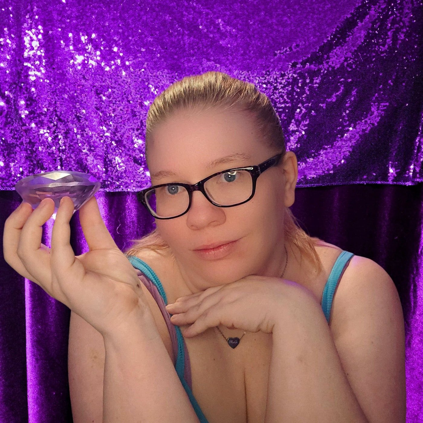 Marie, founder of Marie Glow Studio, holding a purple crystal in front of a purple sequin backdrop